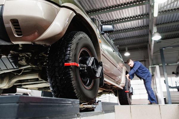 Wheel Alignment specialists for European cars in Denver, CO. Image of mechanic performing a wheel alignment on a tan luxury vehicle.