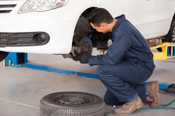 ABS service, diagnostics and repair in Denver, CO at AutoImports of Denver. Image of mechanic knelt down on one knee while checking the brake system on a white sedan in the shop